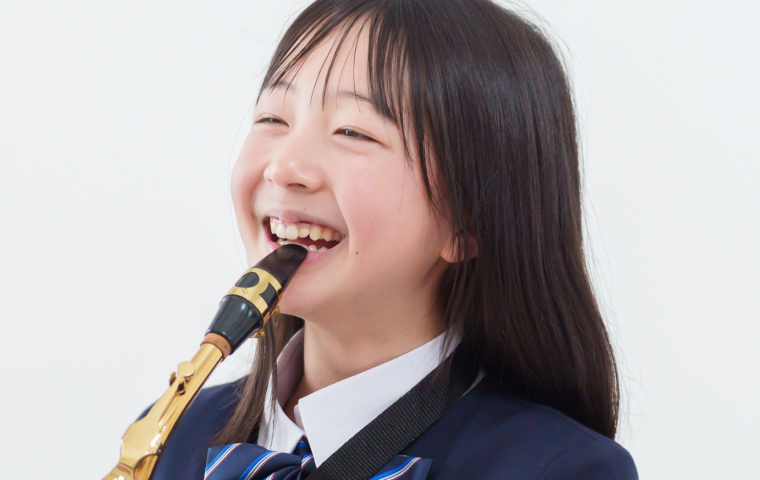 制服を着た女子生徒が笑顔でサックスを吹いている。